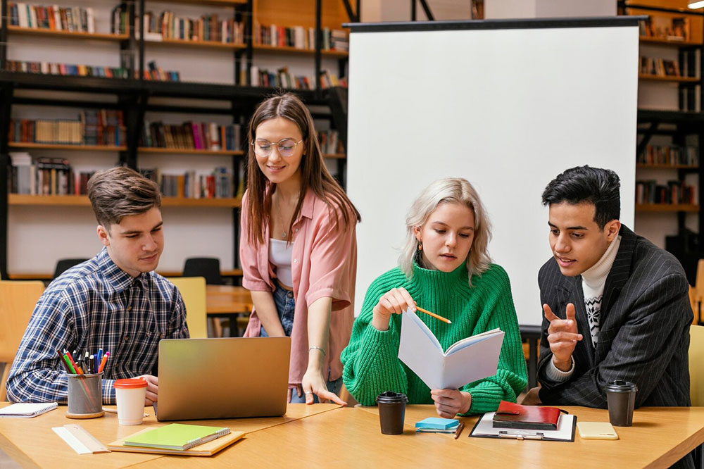 Students collaborating around a laptop and notes at a table in a university library