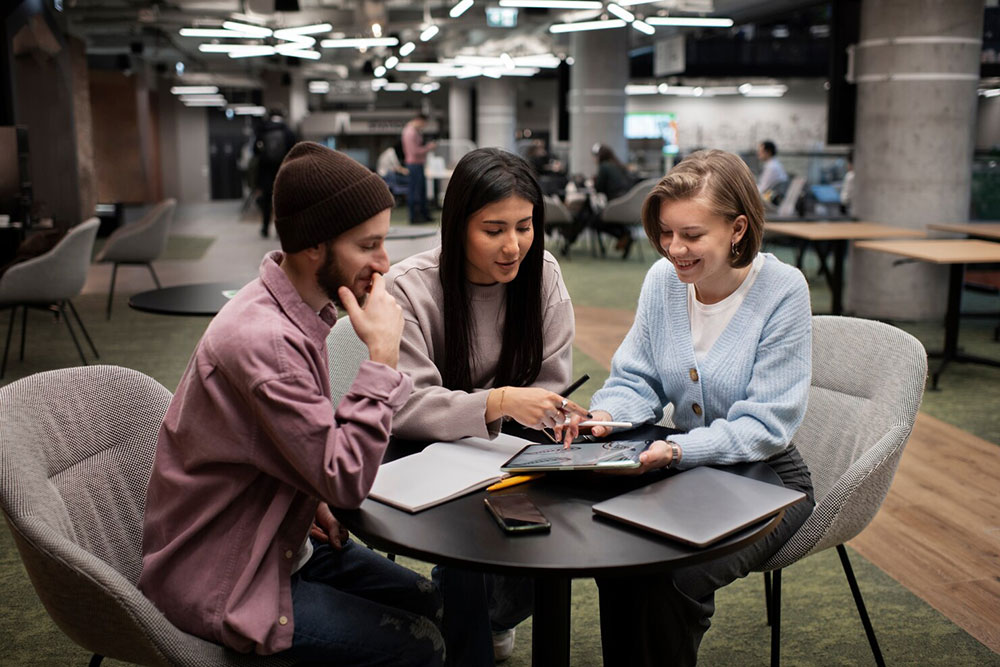 Three students working through student-services tasks together on a tablet and laptop in a campus commons